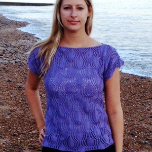 May include: A woman wearing a purple knitted top with a lacy pattern, standing on a beach.