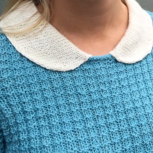 May include: A light blue knitted sweater with a white Peter Pan collar.