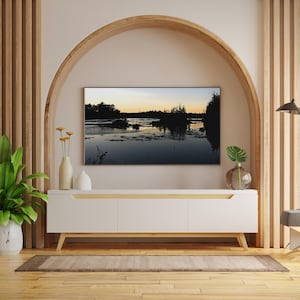 Könnte beinhalten: Ein modernes Wohnzimmer mit einem weißen Schrank, einem großen Fernseher mit einer Landschaft und dekorativen Vasen. Der Raum verfügt über Holzakzente, eine grüne Pflanze und eine Stehlampe, die eine stilvolle und einladende Atmosphäre schaffen.