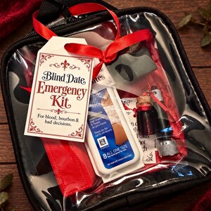 May include: A black zippered pouch with a clear front containing a Blind Date Emergency Kit. The tag reads: Blind Date Emergency Kit. For blood, bourbon & bad decisions. Inside are a white bandage box, a small glass vial, and a metal tool.