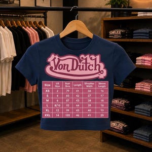 May include: A dark blue short-sleeved t-shirt featuring a pink Von Dutch logo and a size chart printed on the front. The chart lists measurements for sizes XS through XXL, including US size, bust size, length, shoulder width, and sleeve length.