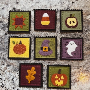 May include: Eight square felt patches with scalloped edges featuring autumn and Halloween motifs: a star, candy corn, an apple slice, a pumpkin, a witch hat, a ghost, an oak leaf, and a jack-o'-lantern in shades of orange, green, and purple.