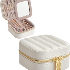 May include: A white, quilted jewelry box with a gold zipper and a square mirror inside. The open box reveals compartments for rings, earrings, and necklaces. The jewelry box is shown open and closed.