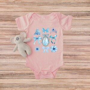 May include: A pale pink baby bodysuit decorated with blue watercolour illustrations of a castle, bows, a tiara, flowers, and a princess portrait. A plush koala toy is next to the bodysuit.