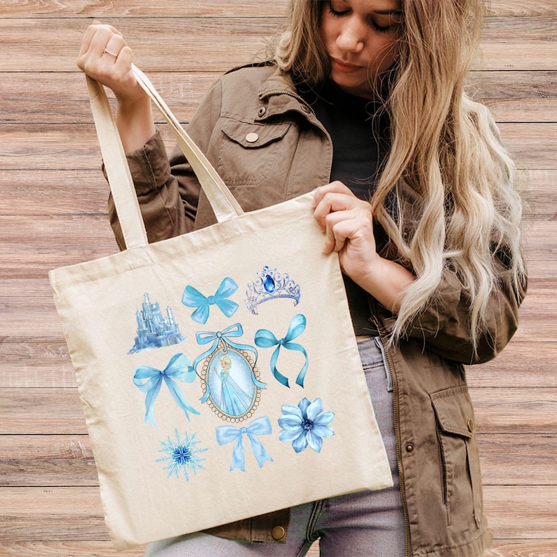 May include: A cream-coloured tote bag displaying watercolour illustrations of a blue castle, bows, a tiara, a snowflake, a flower, and a princess portrait. The bag has cream handles and is made of a durable fabric.