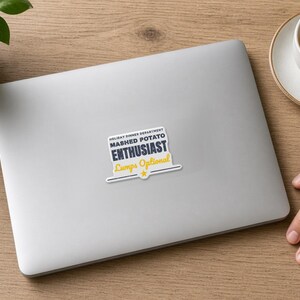 May include: A rectangular sticker with a white background and dark blue text that reads HOLIDAY DINNER DEPARTMENT MASHED POTATO ENTHUSIAST. Below this, the text Lumps Optional is written in yellow script, followed by a horizontal line and a star.