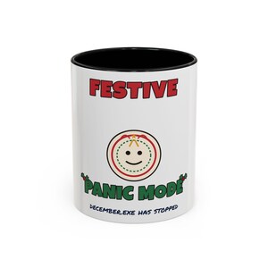 May include: A white ceramic mug with a black interior and rim. The front features the red text FESTIVE, a circular graphic of a smiling face, the green text PANIC MODE with holly accents, and the blue text DECEMBER.EXE HAS STOPPED.
