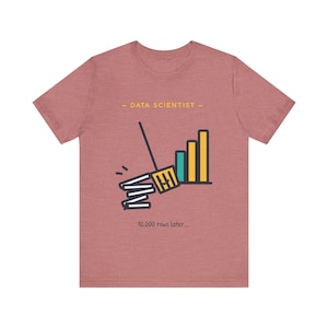 May include: A heathered mauve short-sleeve t-shirt featuring a graphic of a broom sweeping a stack of papers into a bar chart. The text reads "DATA SCIENTIST" at the top and "10,000 rows later..." at the bottom in a simple dark font.