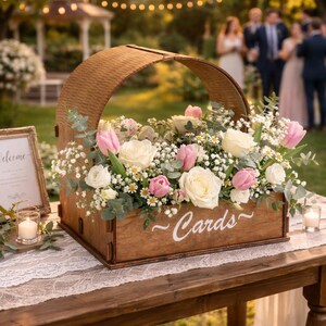 Könnte beinhalten: Eine Holzkartenbox mit gebogenem Griff, gefüllt mit weißen und rosa Rosen, Tulpen und Schleierkraut. Die Box steht auf einem Holztisch mit einem Spitzentischläufer, mit dem Wort "Cards" auf der Vorderseite.