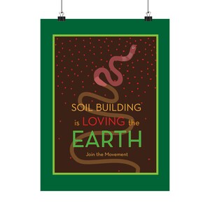 May include: A rectangular poster with a dark brown background and a green border. A pink earthworm curves upward through small red hearts. The text reads: SOIL BUILDING is LOVING the EARTH. Join the Movement. The design is framed by a dark green border.