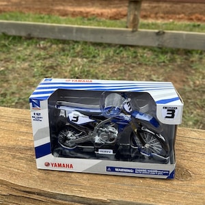 K&ouml;nnte beinhalten: Blau-schwarzes Yamaha Motorradmodell in einer transparenten Kunststoff-Vitrine. Das Modell hat die Nummer 3 und den Namen "DUFFY". Die Box tr&auml;gt das Yamaha-Logo und den Text "1:12 Die-Cast Plastic".