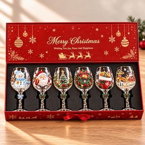 May include: A red rectangular gift box containing six clear wine glasses, each decorated with distinct Christmas motifs including a snowman, Santa Claus, a tree, a wreath, a stocking, and a sleigh. The box lid features gold text reading Merry Christmas.