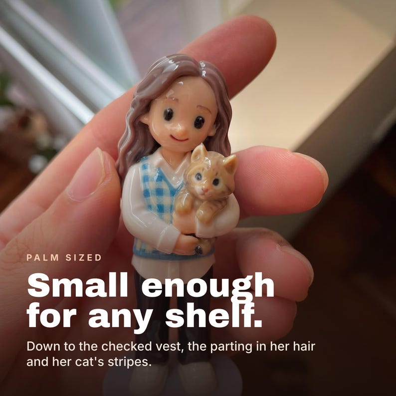 May include: A small figurine of a person with long wavy hair wearing a white shirt and a blue and white checkered vest, holding a small orange tabby cat. The text on the image reads: PALM SIZED Small enough for any shelf. Down to the checked vest, the parting in her hair and her cat's stripes.