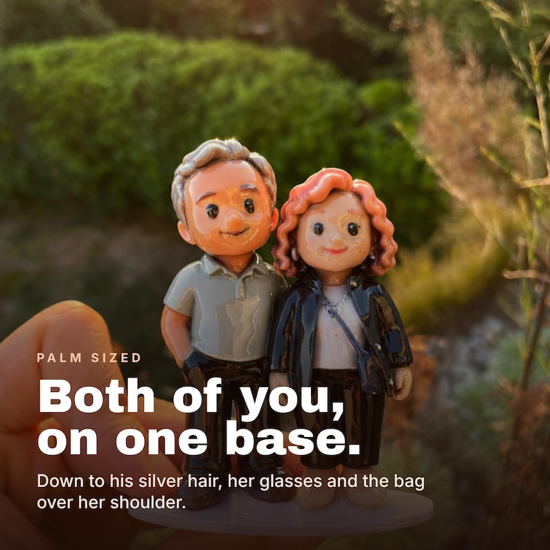 May include: A custom figurine of a couple standing on a single base. The male figure has silver hair and wears a grey polo shirt with dark pants. The female figure has curly reddish-brown hair, wears glasses, a white top, black jacket, and a shoulder bag.