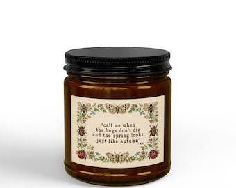 Puede incluir: Un tarro de vela de vidrio marrón con tapa negra y una etiqueta rectangular. La etiqueta presenta un fondo crema con un borde botánico de insectos y flores, y el texto: "call me when the bugs don't die and the spring looks just like autumn" - M.K.