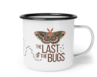Puede incluir: Taza de esmalte blanco con borde y asa negros. La taza presenta una colorida ilustración de una polilla sobre el texto "THE LAST OF THE BUGS" en marrón. Una línea punteada de hormigas está en el lado izquierdo de la taza.