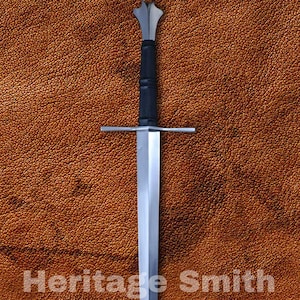 May include: A long, silver sword with a black handle and crossguard, set against a textured brown background. The text "Heritage Smith" is displayed on the surface.