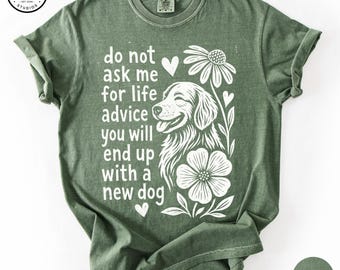 May include: A moss green short-sleeve t-shirt featuring a white graphic print of a dog, flowers, and hearts. The text reads: do not ask me for life advice you will end up with a new dog. The shirt has a crew neckline and a relaxed fit.