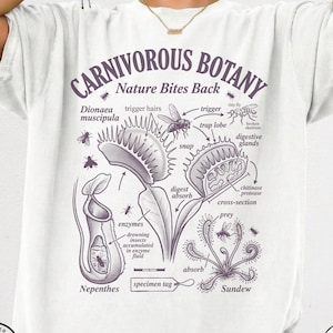 May include: A white t-shirt featuring a dark purple botanical diagram titled CARNIVOROUS BOTANY Nature Bites Back. The graphic illustrates a Venus flytrap, pitcher plant, and sundew with labels like trigger hairs, digestive glands, and enzymes.
