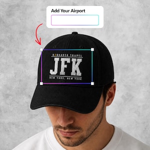 Op de afbeelding: Een zwarte honkbalpet met witte geborduurde tekst die R2QUARED TRAVEL, JFK en NEW YORK, NEW YORK leest. Boven de pet staat een wit rechthoekig vak met de tekst Add Your Airport en daaronder een leeg invoerveld.