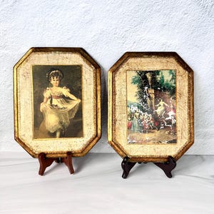 May include: Two octagonal wall plaques featuring gold-toned, distressed frames. The left plaque displays a portrait of a child in a light-colored dress. The right plaque depicts an outdoor scene with figures in a garden setting. Both are on stands.