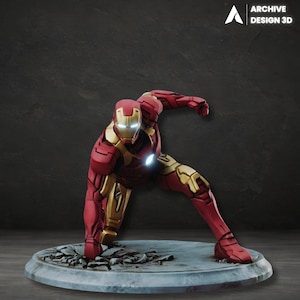 May include: A red and gold Iron Man figurine in a dynamic pose, kneeling on a gray circular base with a cracked surface. The figurine has glowing white eyes and chest piece. The Archive Design 3D logo is in the top right corner.