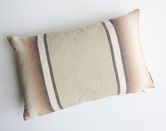 May include: A beige pillow with brown and white stripes. The pillow has a zipper closure on the side.