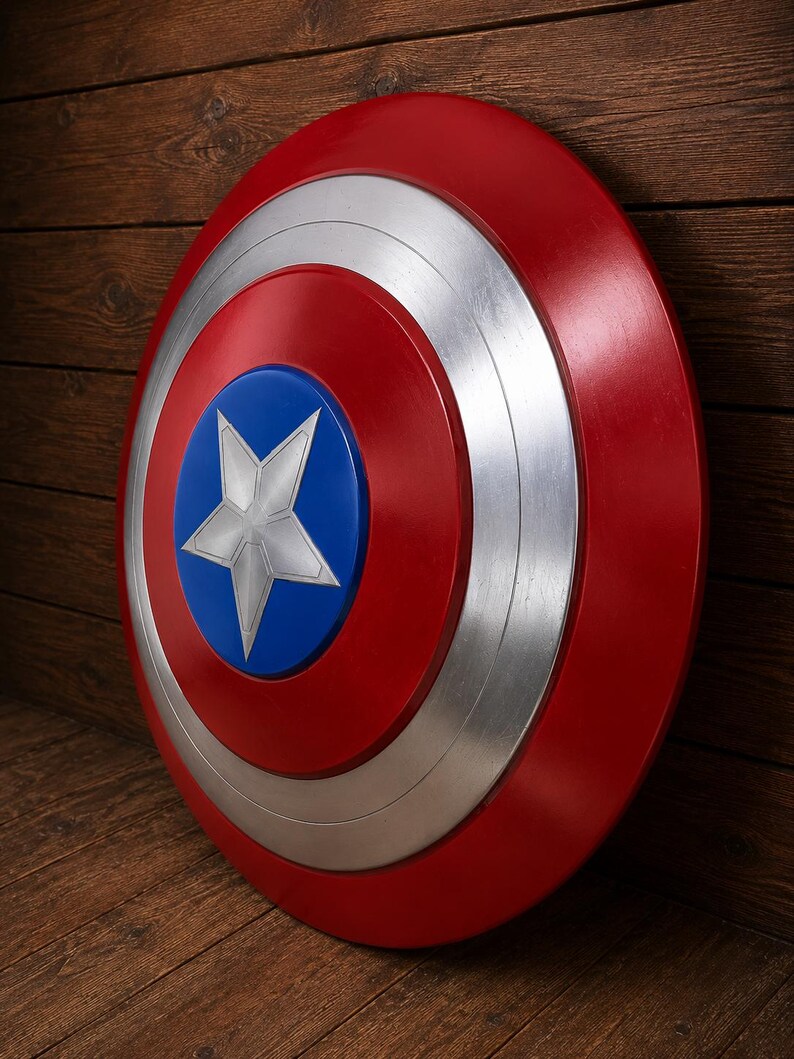 May include: A red, white, and blue shield with a star emblem. The shield has a circular design with a red outer ring, a silver middle ring, and a blue center with a white star. The shield is leaning against a wooden surface.