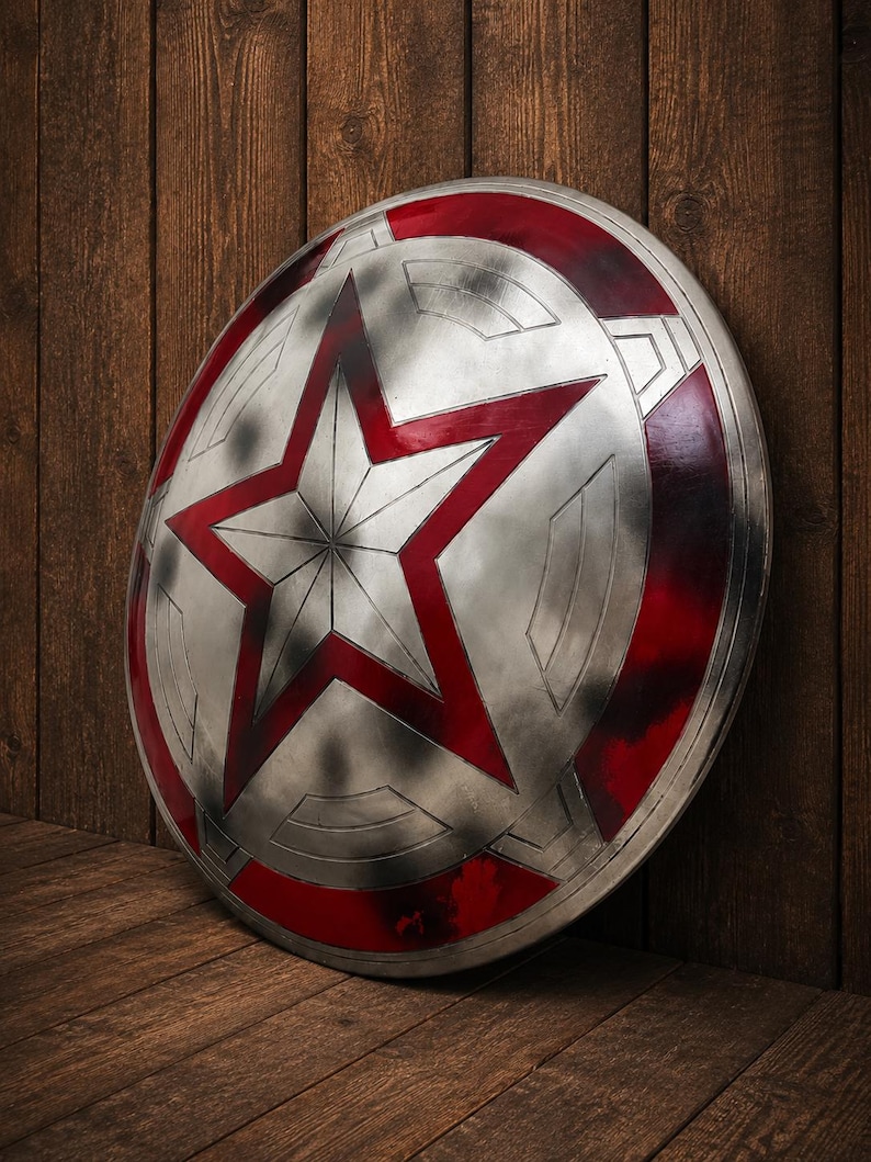 May include: A silver shield with a large red star in the center and red accents around the edge. The shield is leaning against a wooden wall and floor, creating a rustic backdrop.