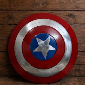 May include: A round shield with a red outer ring, a silver inner ring, and a blue center with a silver star. The shield is set against a wooden background.