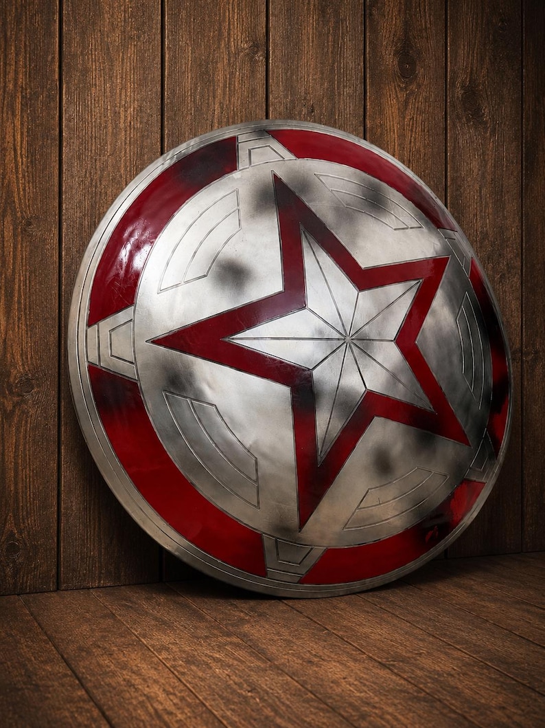 May include: A silver and red shield with a large red star in the center. The shield has a circular design with red accents and a weathered appearance. The shield is leaning against a wooden surface.
