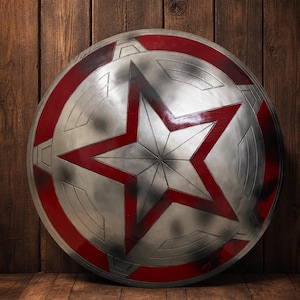 May include: A silver and red shield with a large red star in the center. The shield has a circular design with a red border and is leaning against a wooden background. The shield is approximately 24 inches in diameter.