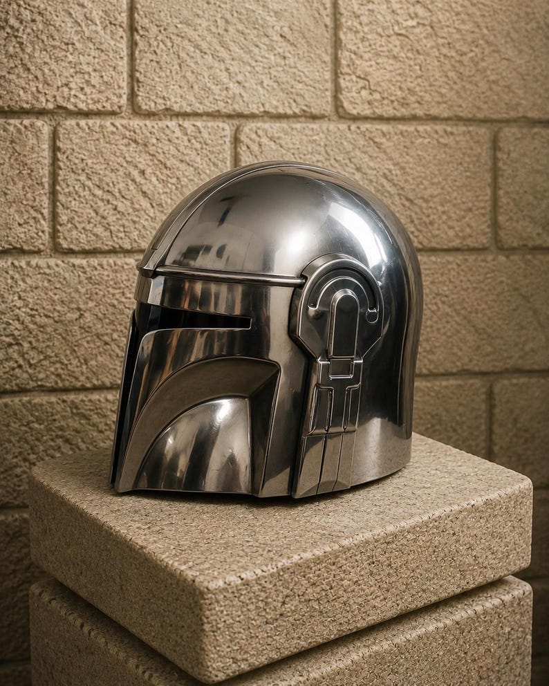 K&ouml;nnte beinhalten: Ein gl&auml;nzender, silberner Helm mit Visier und markanten Seitendetails, der auf einem strukturierten, hellbraunen Block ruht. Das Design des Helms weist eine glatte, metallische Oberfl&auml;che auf, die das Licht reflektiert. Der Helm ist ein Requisit oder Sammlerst&uuml;ck.