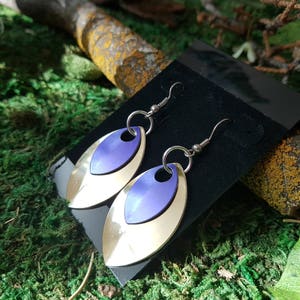 Peut inclure: Une paire de boucles d'oreilles pendantes argentées et violettes avec un design ovale superposé. Les boucles d'oreilles sont présentées sur un fond de velours noir.