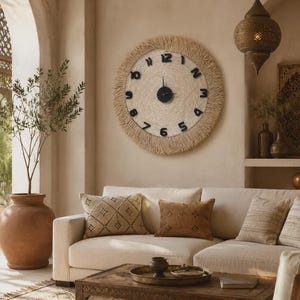 Peut inclure: Une horloge murale ronde avec un centre texturé couleur crème, une bordure beige à franges et des chiffres noirs en relief. L'horloge possède un mécanisme central noir avec de fines aiguilles noires, fixée au mur au-dessus d'un canapé.