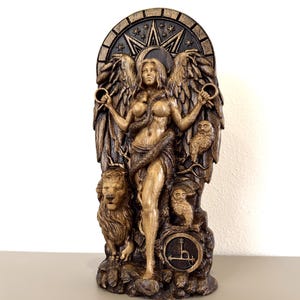 Puede incluir: Una placa de pared tallada en tonos oscuros que presenta una figura alada central que sostiene dos anillos y está envuelta por una serpiente. La figura está flanqueada por un león a la izquierda y un búho a la derecha, sobre un fondo con una estrella, una luna creciente y un símbolo circular.