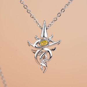 May include: A silver-toned metal pendant necklace featuring an intricate, swirling design with a central oval-shaped yellow gemstone. The pendant hangs from a delicate silver-toned chain, showcasing a polished finish and symmetrical metalwork.