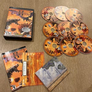 May include: EverQuest II PC game set including a black game case, eight circular game discs with orange and brown fantasy artwork, a quick start guide, a promotional insert, and a small map booklet titled The Shattered West and Isle Vornerus.