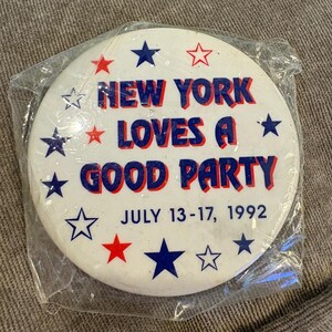 May include: A white button with the text "NEW YORK LOVES A GOOD PARTY" in red and blue. The button is surrounded by red and blue stars and the date "JULY 13-17, 1992". The button is in a clear plastic wrapper.