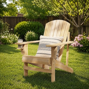 May include: A natural wood Adirondack chair with a built-in cup holder and a decorative pillow. The pillow has a black and white geometric pattern. The chair is on a green lawn, surrounded by trees and bushes.