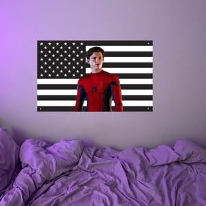 May include: A wall art piece featuring a black and white American flag design with a portrait of a person in a red and blue superhero suit. The artwork is mounted on a wall above a bed with purple bedding.