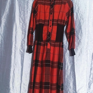 May include: A long-sleeved, red and black checked dress with a high collar and button-down front. The dress has a fitted waist and long sleeves with black cuffs. The checked pattern is a classic design, suitable for vintage or retro fashion.