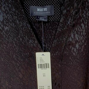 May include: Black patterned top with a V-neck collar. The tag reads "Maeve by ANTHROPOLOGIE" and indicates size XS. The top is made in Vietnam.