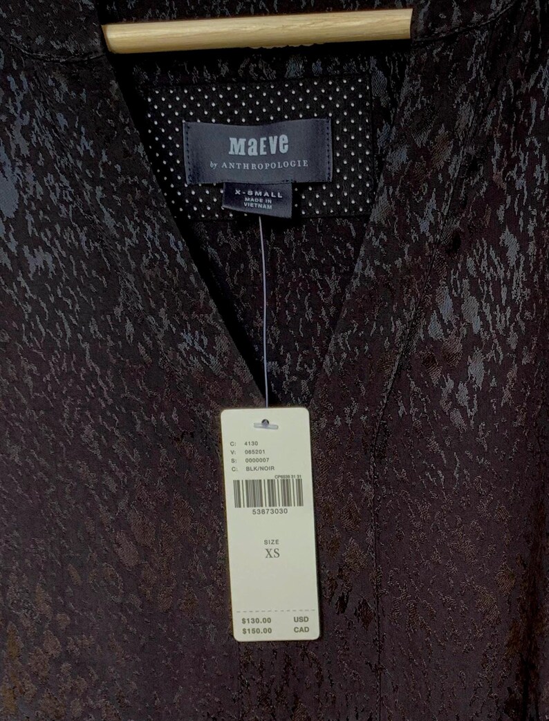 May include: Black patterned top with a V-neck collar. The tag reads "Maeve by ANTHROPOLOGIE" and indicates size XS. The top is made in Vietnam.