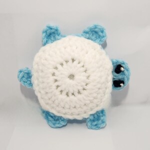 May include: A handmade crochet turtle toy. The turtle has a white shell with a circular pattern and light blue flippers, head, and tail. The eyes are black. This soft toy is suitable for children.