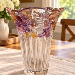 May include: A clear glass vase featuring a flared, scalloped rim and a vertical ribbed base. The upper section is decorated with embossed, frosted glass clusters of grapes and leaves, accented with iridescent purple and amber gold tones.