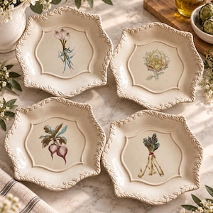 May include: A set of four cream-colored ceramic plates with a scalloped, leaf-embossed rim. Each plate features a unique botanical illustration in the center: a bundle of garlic, an artichoke, two radishes, and a bunch of asparagus stalks.