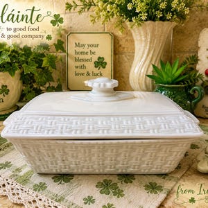 May include: A rectangular white ceramic casserole dish with a lid, featuring a textured basket-weave pattern on the exterior sides and the lid rim. The lid is topped with a central knob handle. The dish has integrated side handles for lifting.