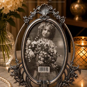 May include: An oval-shaped silver-toned metal picture frame with ornate floral and scrollwork detailing. The frame features a central oval opening containing a black and white photograph of a child holding flowers, with a 5 inch by 7 inch label.