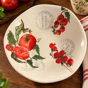 May include: A white ceramic bowl featuring a botanical illustration of red tomatoes on vines and green leaves. The design includes two circular vintage-style stamps with the text REGIMENT DE TIRailleurs CONSEIL D'ADMINISTRATION in black ink.